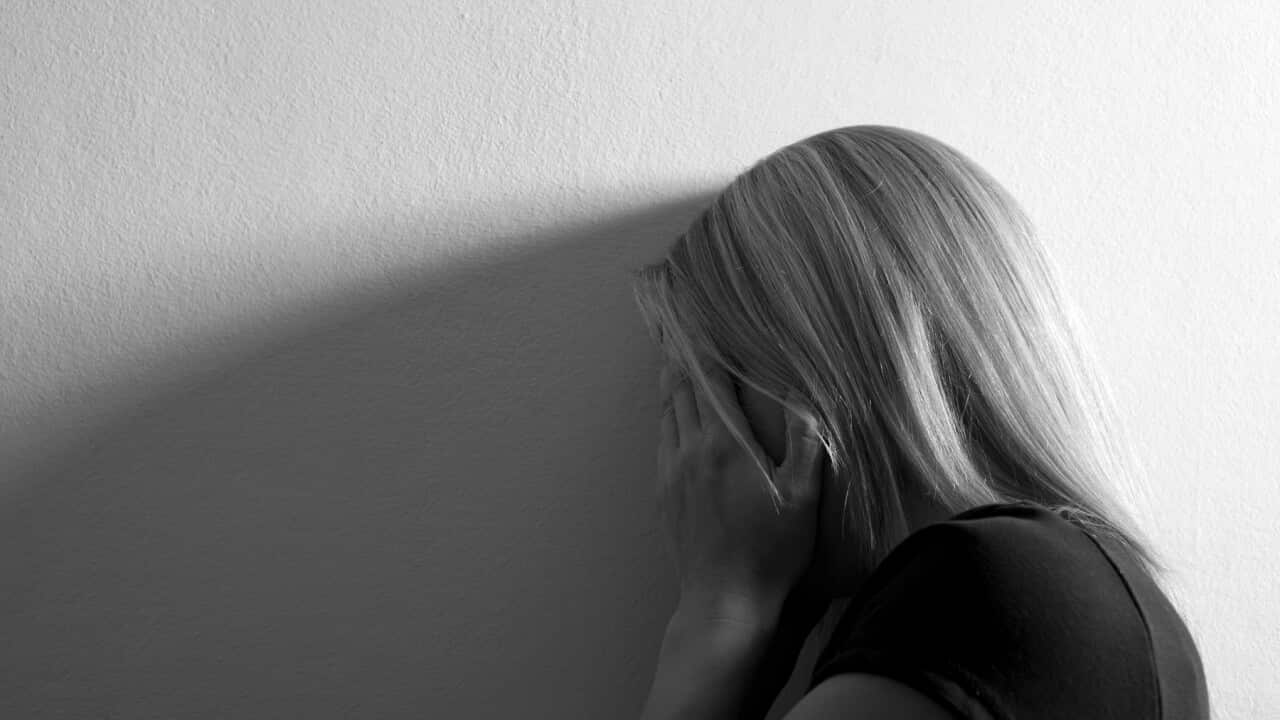 Sad woman with hands on her face leaning on wall
