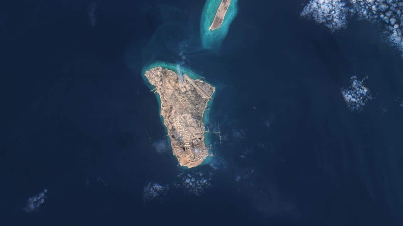 An aerial satellite view of a teardrop-shaped island surrounded by deep blue water and light turquoise coral reefs.