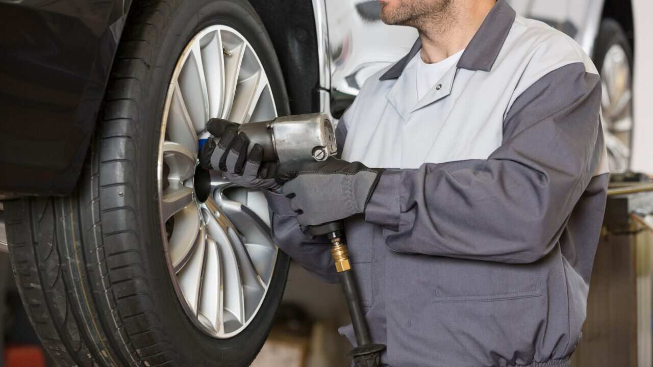 Midsection of male mechanic repairing car's wheel in workshop