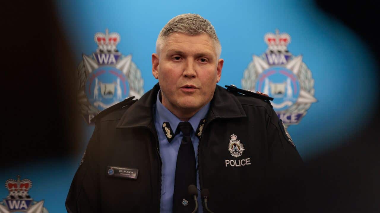 A man wearing a police uniform, standing in front of a blue wall with the WA Police logo.