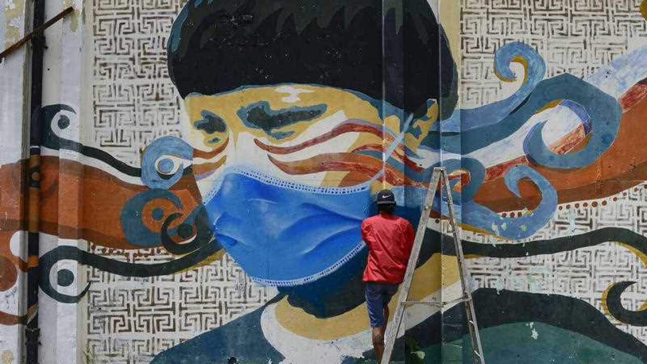 A street artist spray paints a protective face mask over an old mural featuring a Venezuelan Indigenous man, in Caracas, Venezuela, Saturday, July 18, 2020,