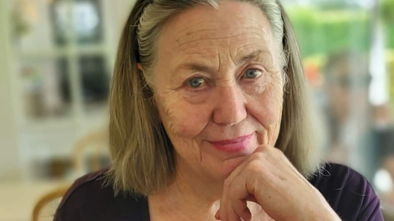 An elderly woman sits at the table, holding her chin with her left hand.
