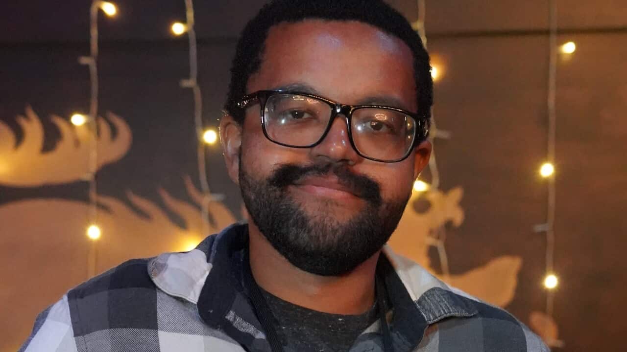 A man wearing a plaid shirt and glasses holding a card up.