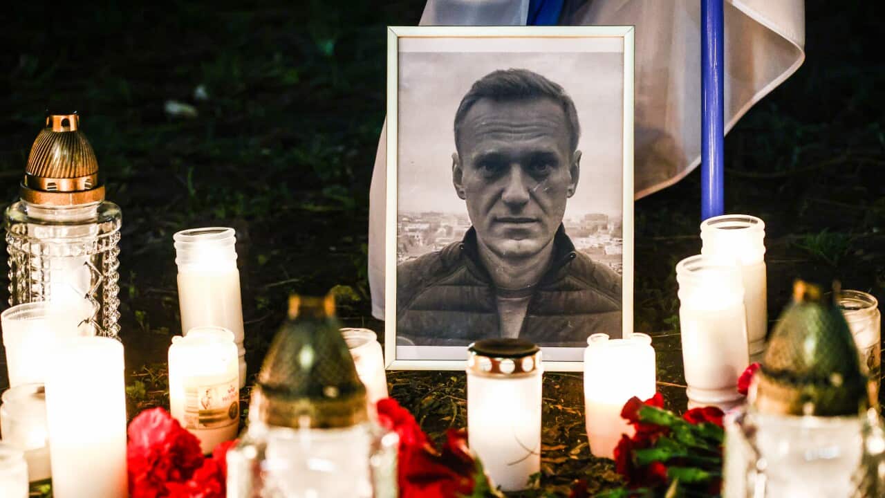Candles and flowers are placed in front of a framed photo of a man.