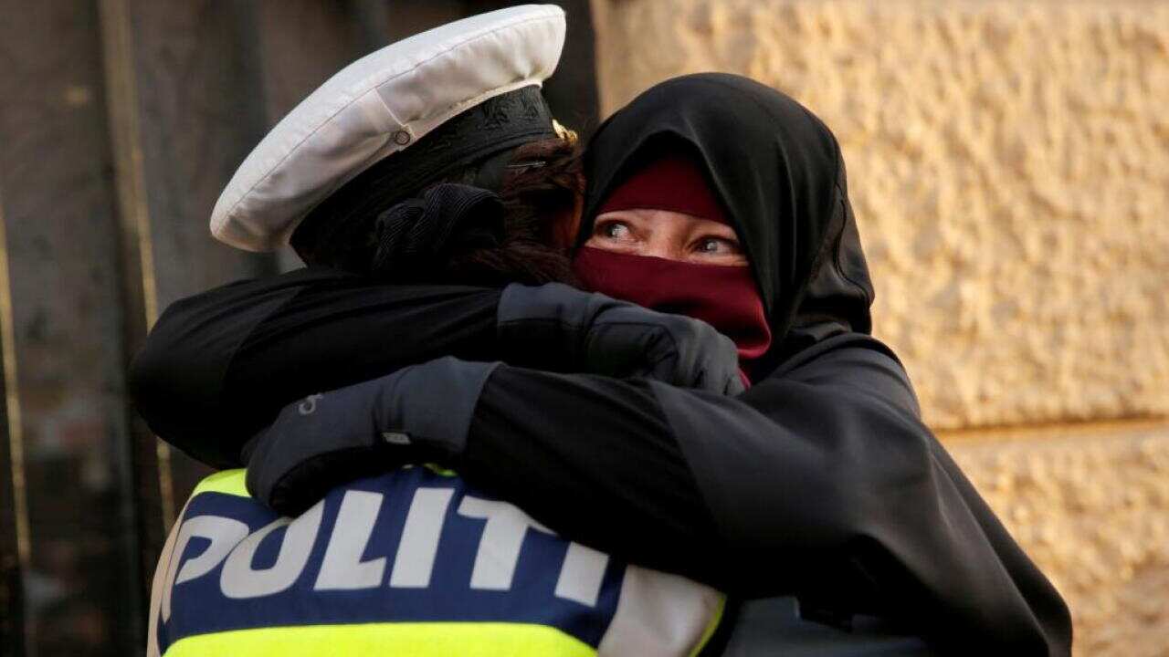 Policewoman hugging veiled woman.