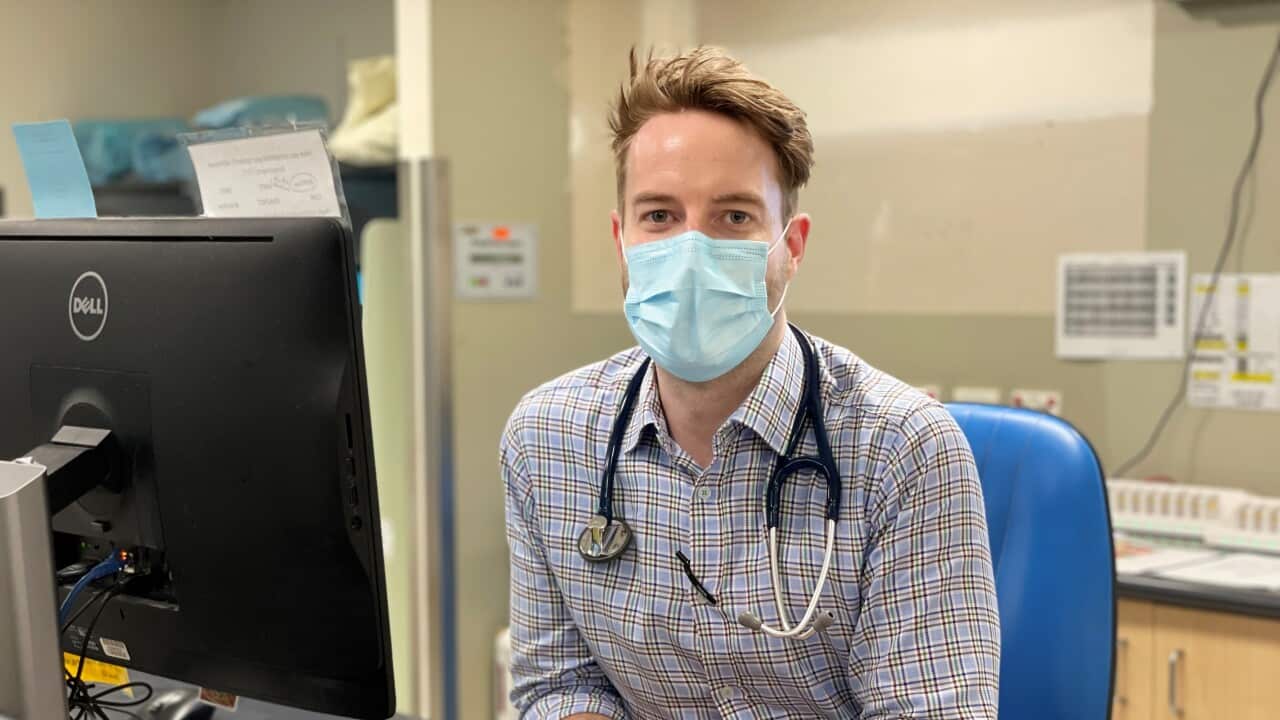 A man sitting in a medical office with a stethoscope around his neck and a surgical mask on his face.