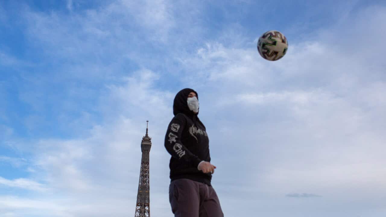 A young man wears a mask to protect against the spread of the coronavirus as he plays with a soccer ball close to the Eiffel Tower in Paris.