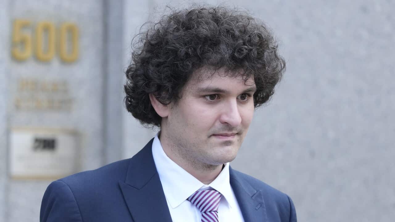 A man with curly hair staring down wearing a suit.