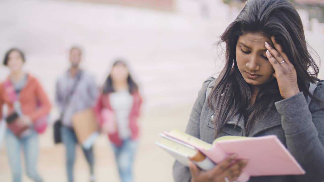 Sad female college student holding her head and reading book.