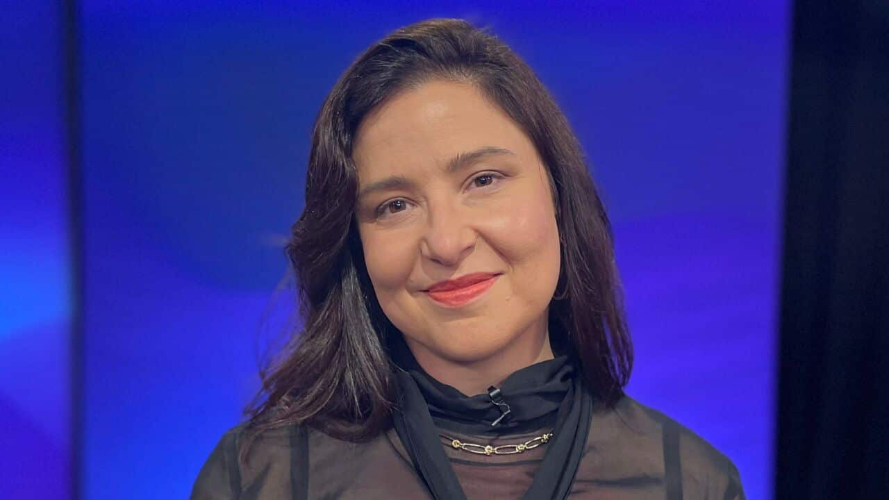a woman with long brown hair wearing a black sheer top in front of a blue and black background