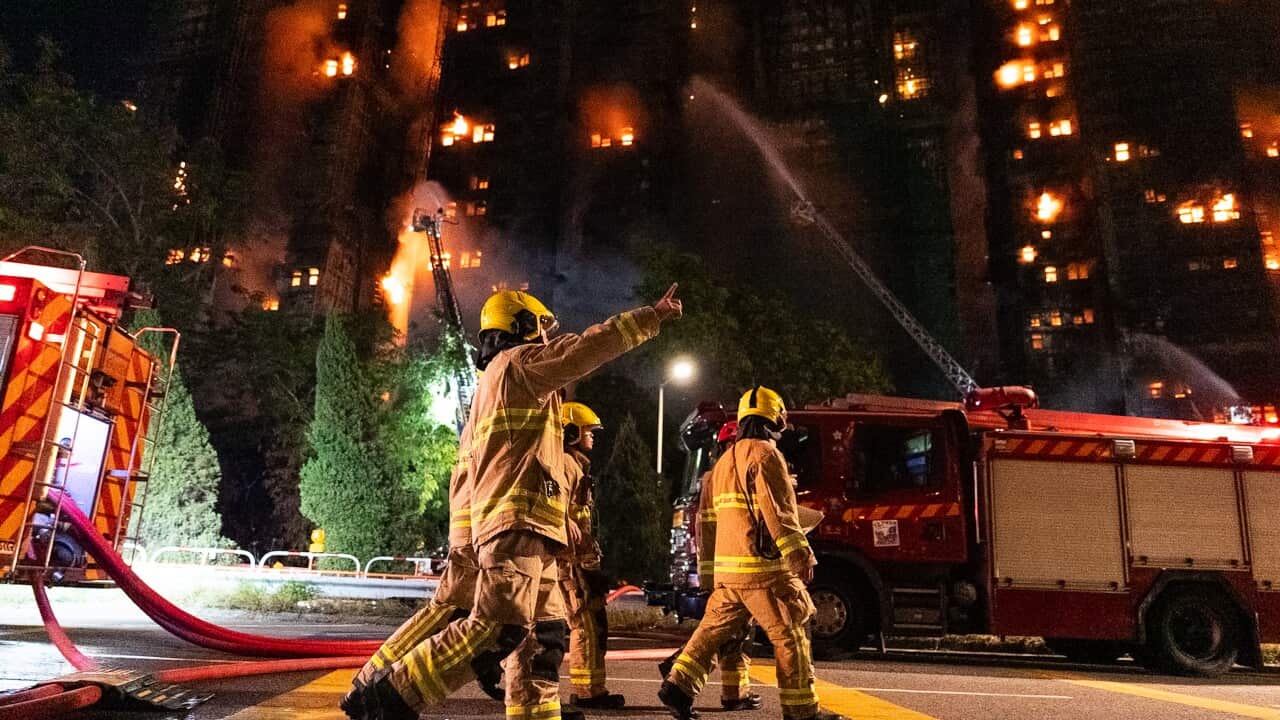 Firefighters standing outside a building complex on fire.