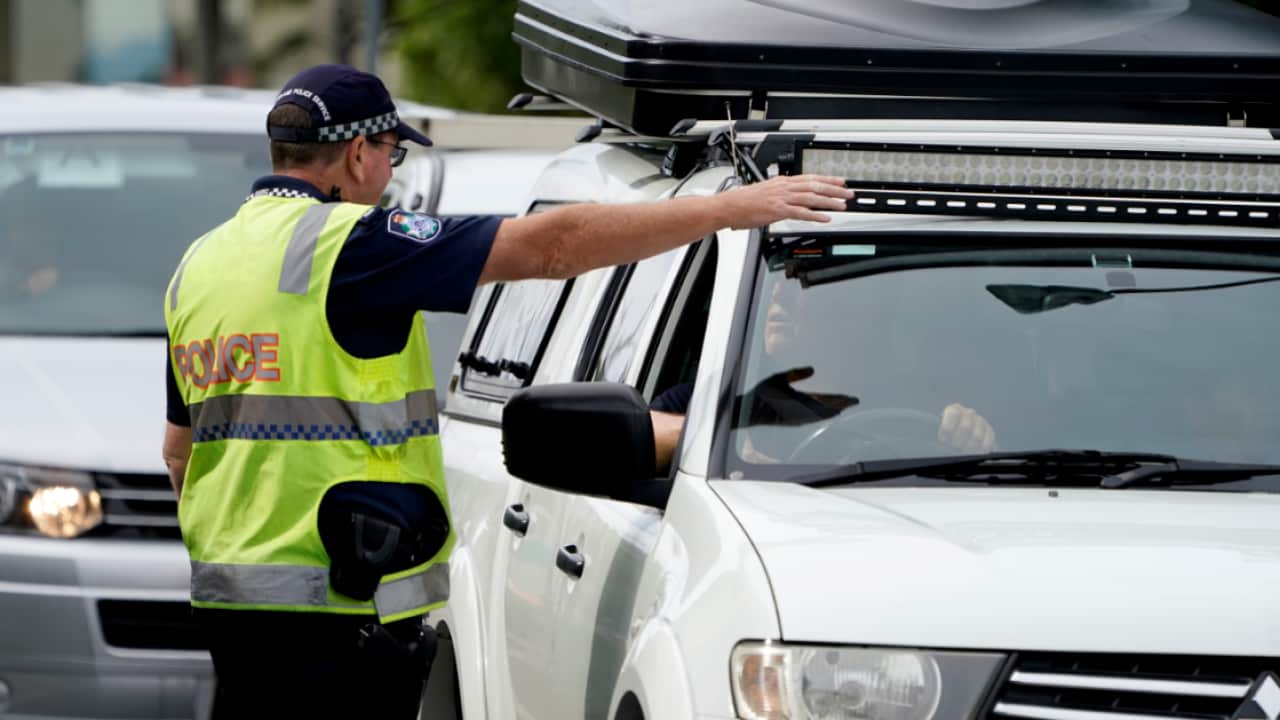 A Queensland police officer gestures for a motorist to pull over at a checkpoint at Coolangatta on the Queensland-New South Wales border, Friday, May 22, 2020