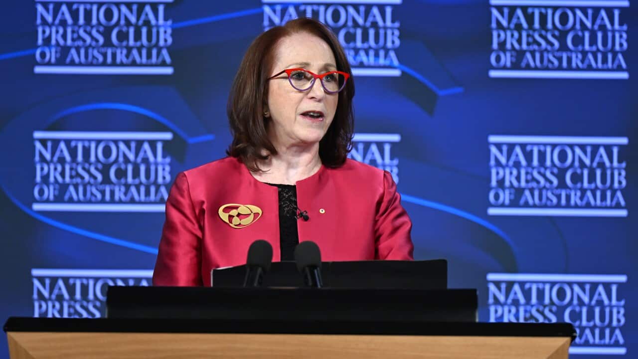 A woman stands in front of National Press Club of Australia signs in red jacket