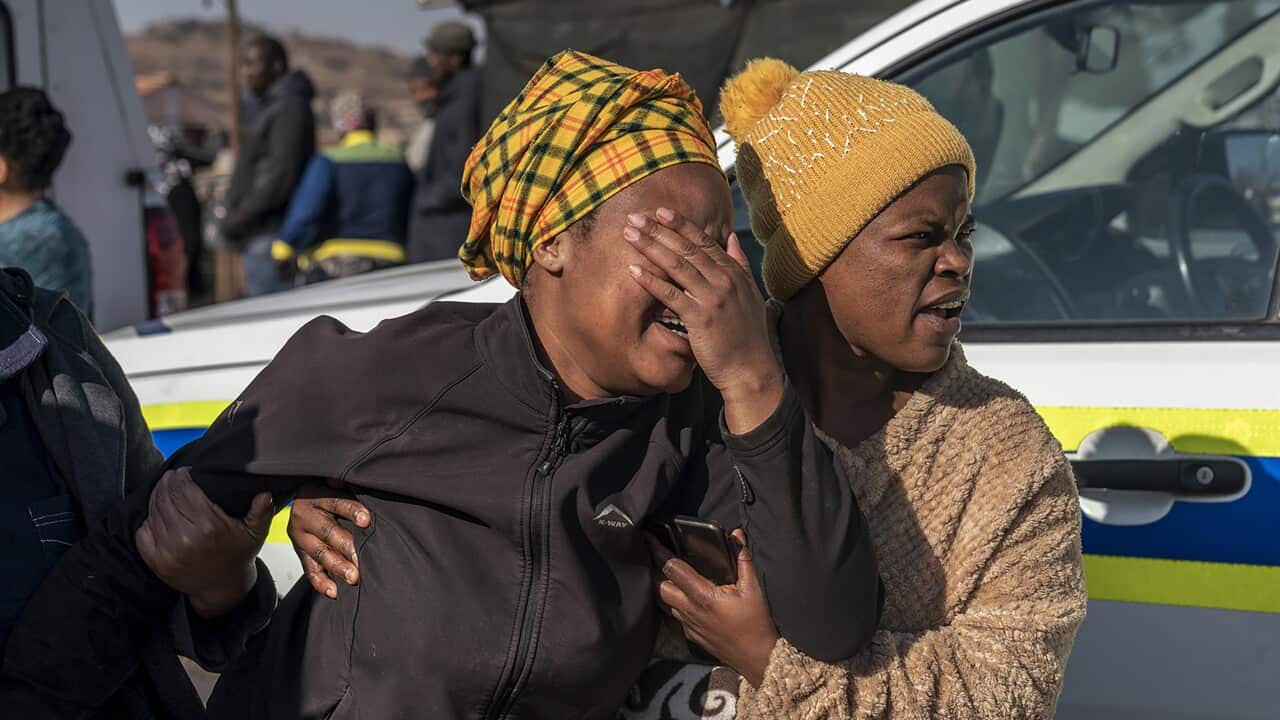 Two women holding onto one another walking out of a building. One is covering her face and looks emotional.