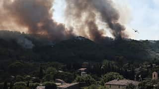 Plumes of black smoke rise from treelined hills next to a small town