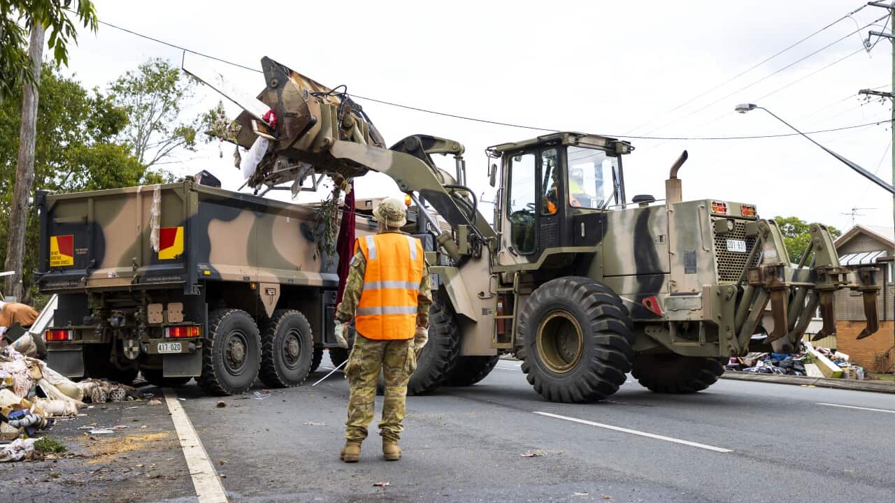 An excavator is seen tipping flood-damaged belongings into a truck.