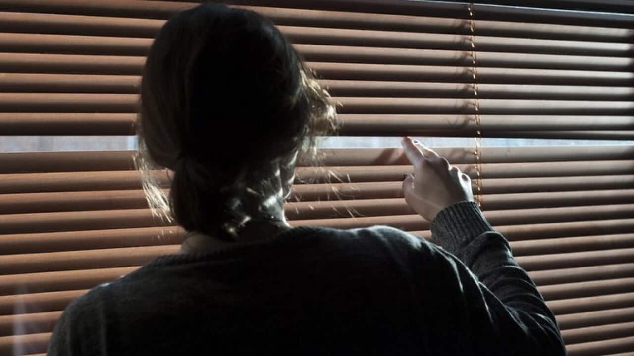 A woman looks out a window through a blind.