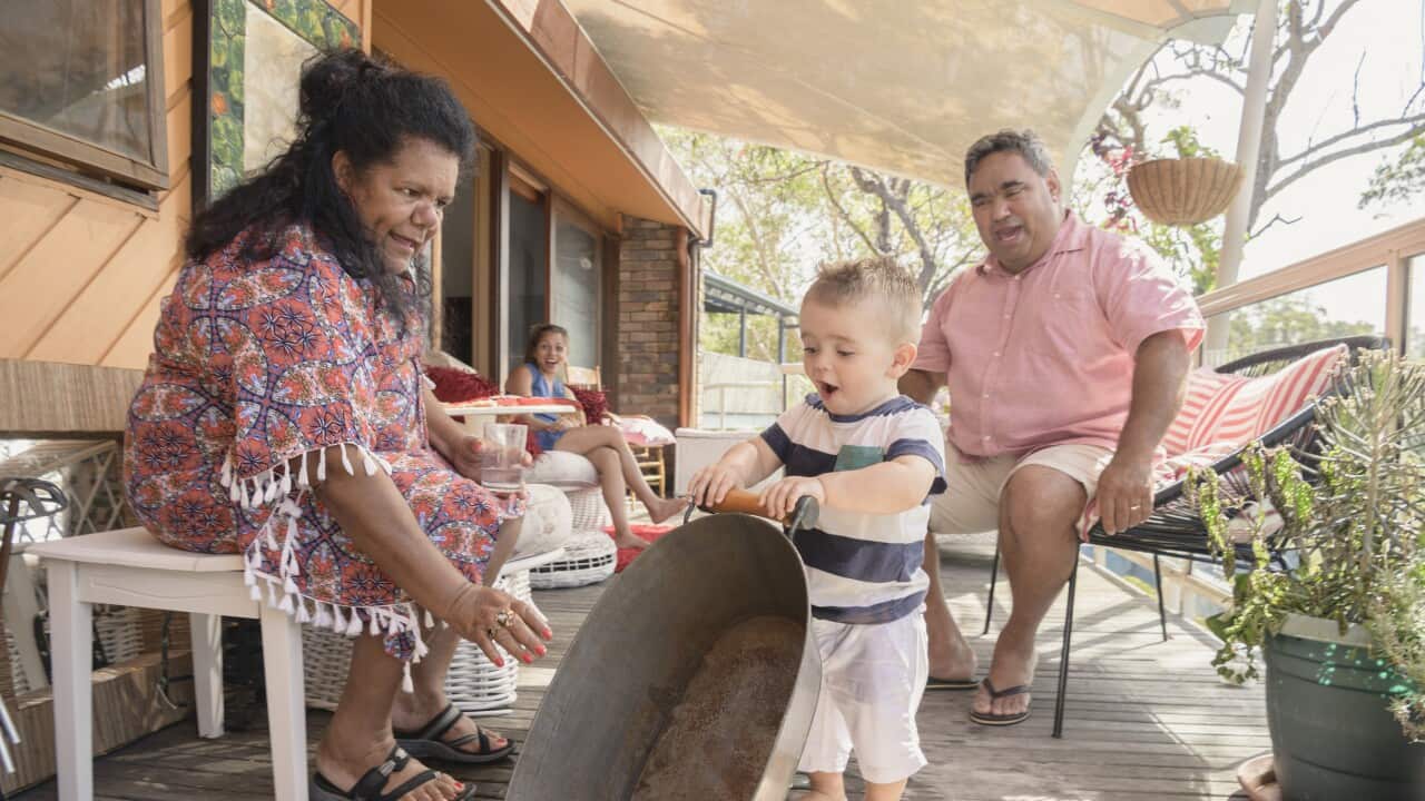 Boy playing with metal baby bath with grandparents on porch