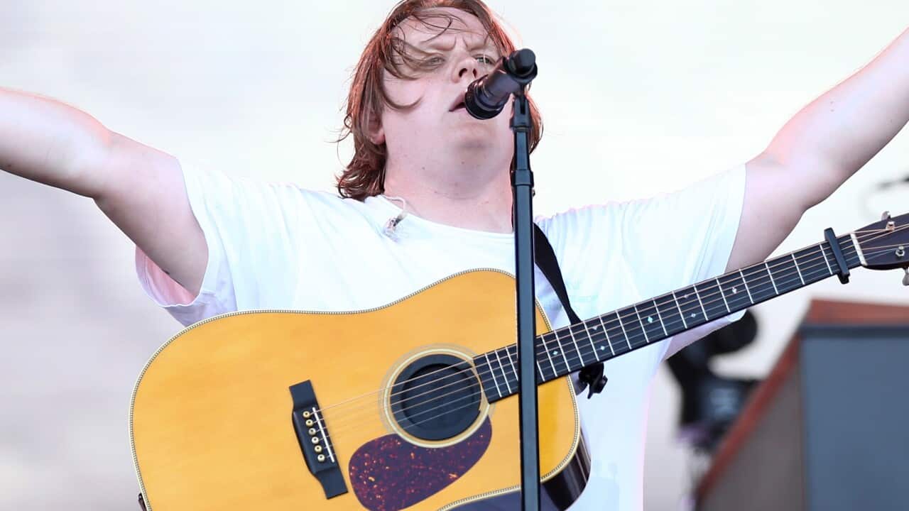 Lewis Capaldi on stage with his arms in the air and guitar slung over his shoulder.