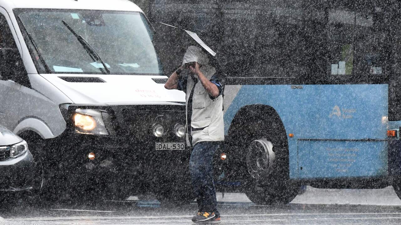 A man with an umbrella walks across a city road