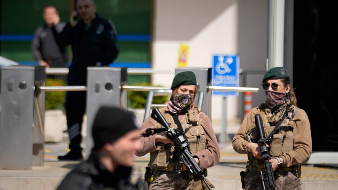 Men in military uniforms holding guns stand near a gate.