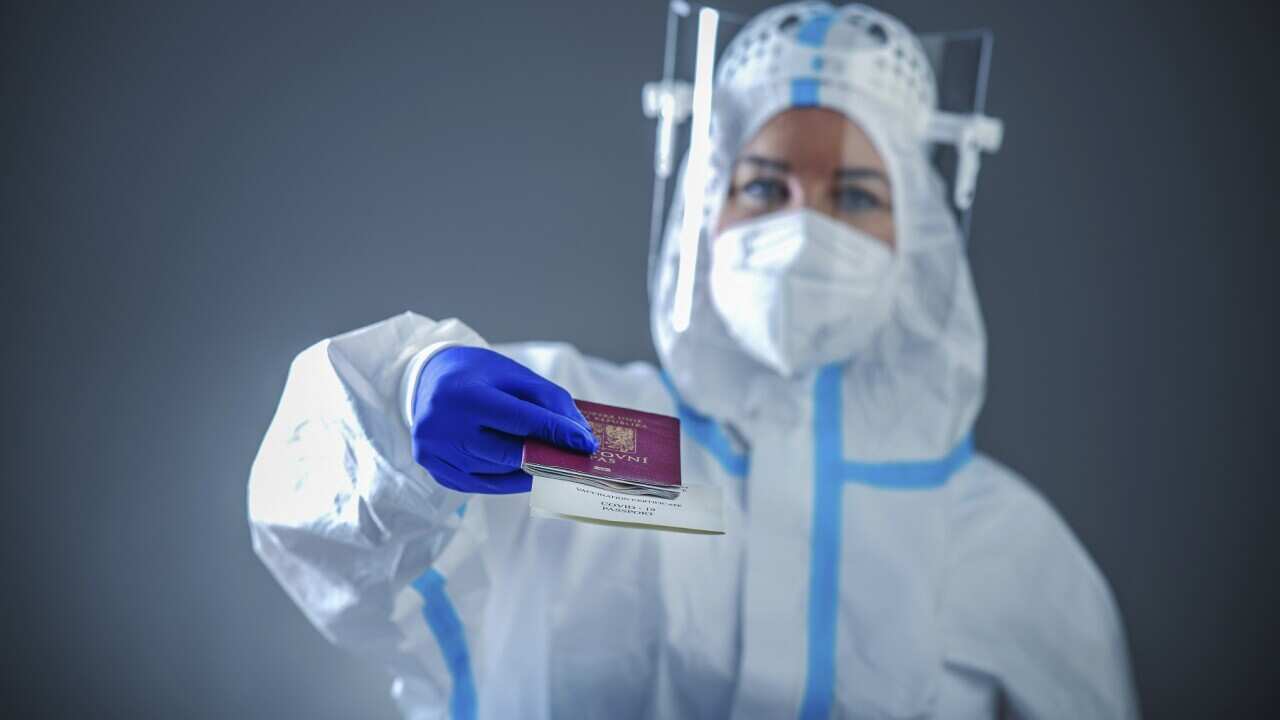 Doctor or medic in a protective suit holding a passport of the Czech Republic with a printed certificate of infectivity on Covid - 19