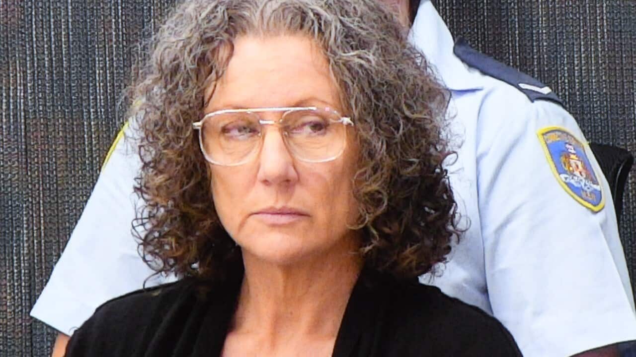 Kathleen Folbigg appears on a video link screen. There is a female officer standing behind her.