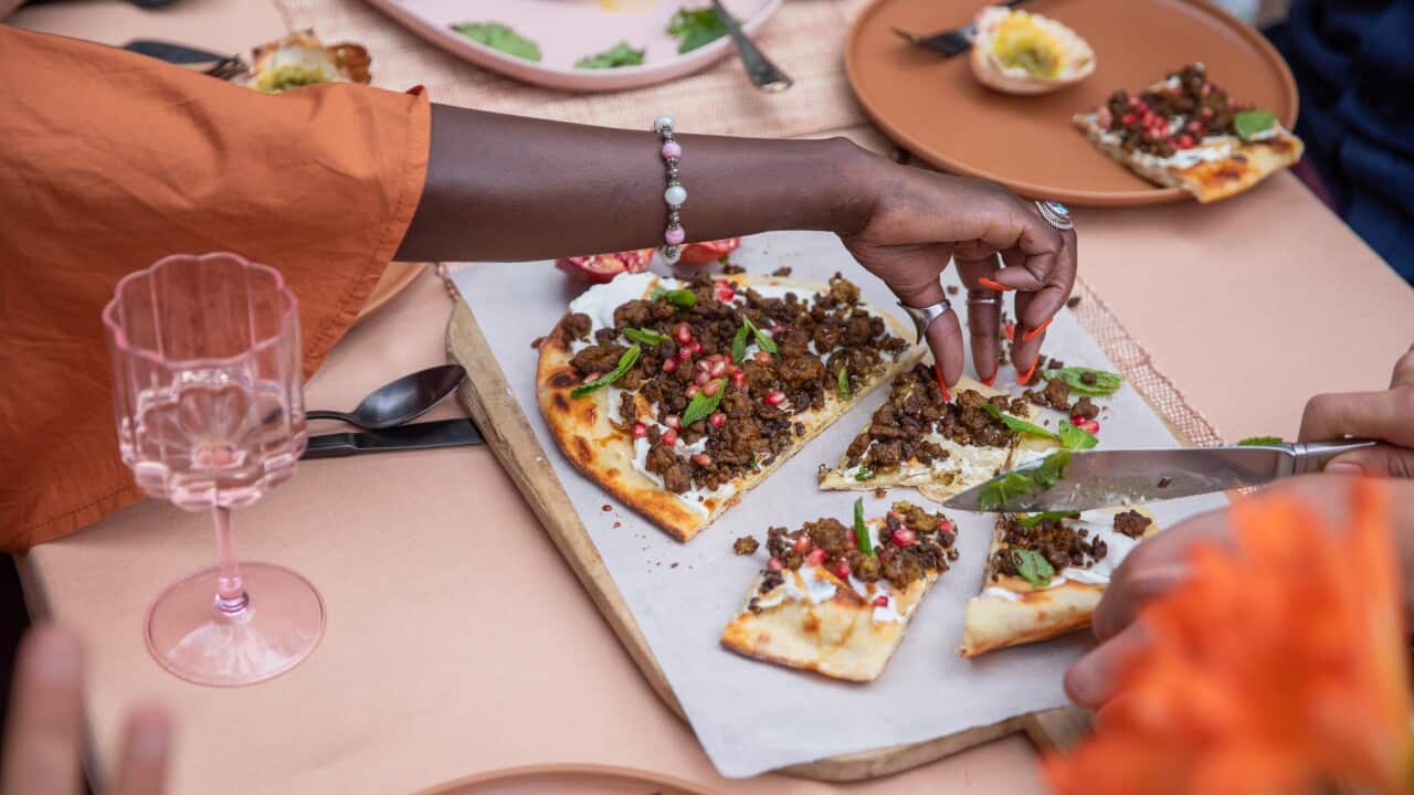 A hand reaches for mouth-watering barbecued lamb flatbreads, cut up on an entertaining table