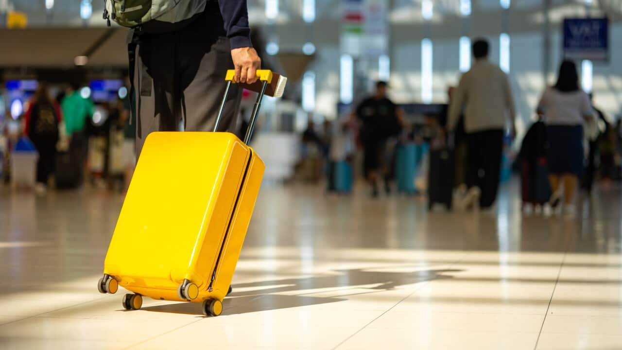 Image of a yellow suitcase being rolled through a busy airport.
