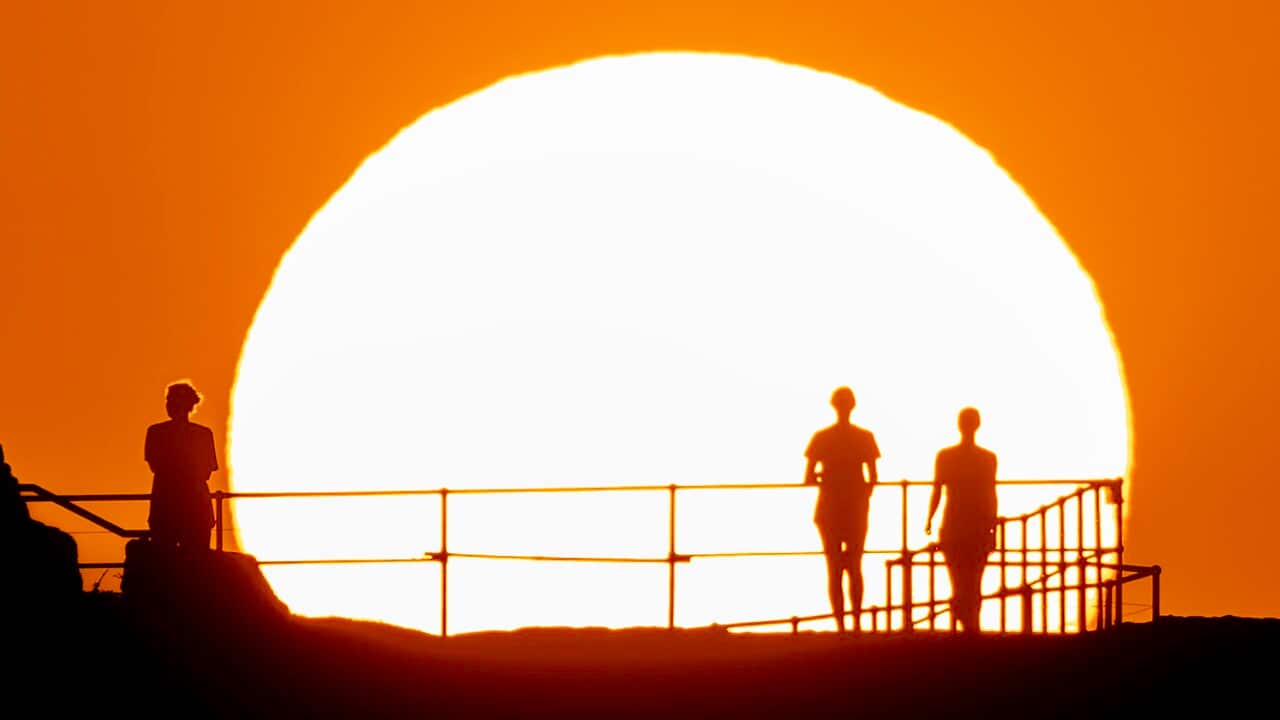 Silhouettes of people against a large, burning white sun in an orange sky.