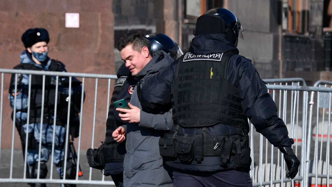 Russian police officers are seen detaining a man during a protest against Russian military action in Ukraine.