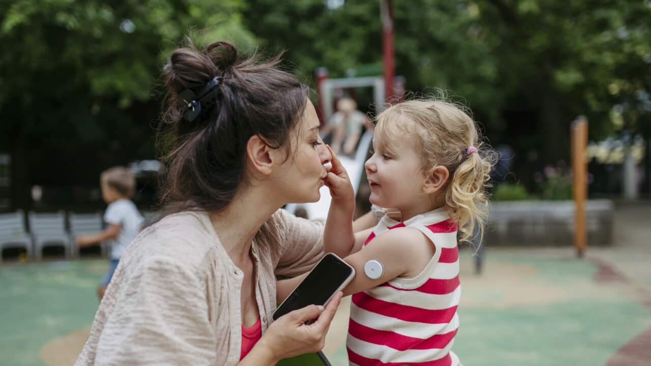 Mother with smartphone checking on little girl with a continuous glucose monitor sensor on her shoulder