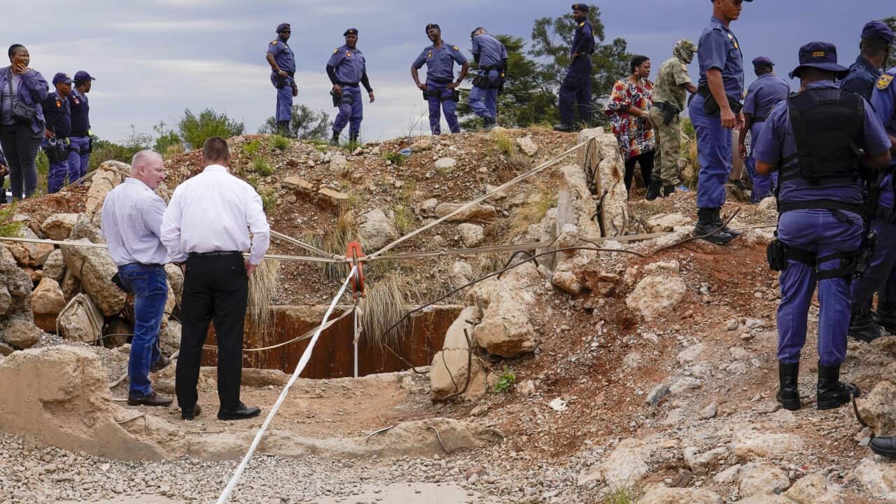 A large group of people, many of them in blue rescue uniforms, standing outside the front of a mine shaft.