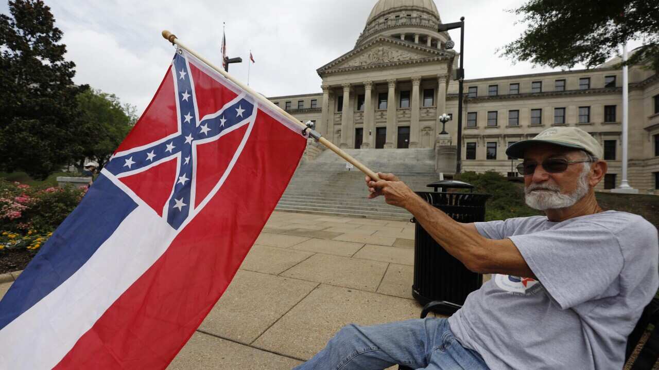 A man waves the current Mississippi state flag outside the Capitol, Saturday, June 27, 2020