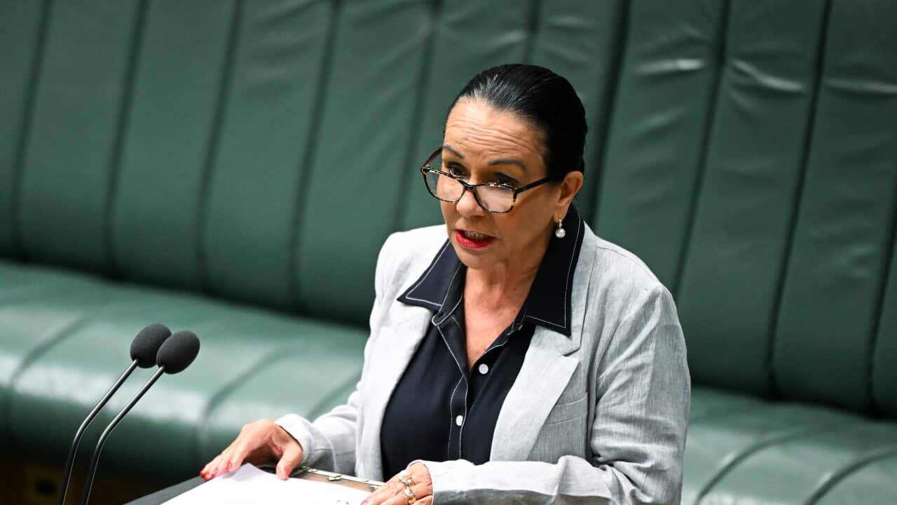 A woman standing and speaking in front of microphones.