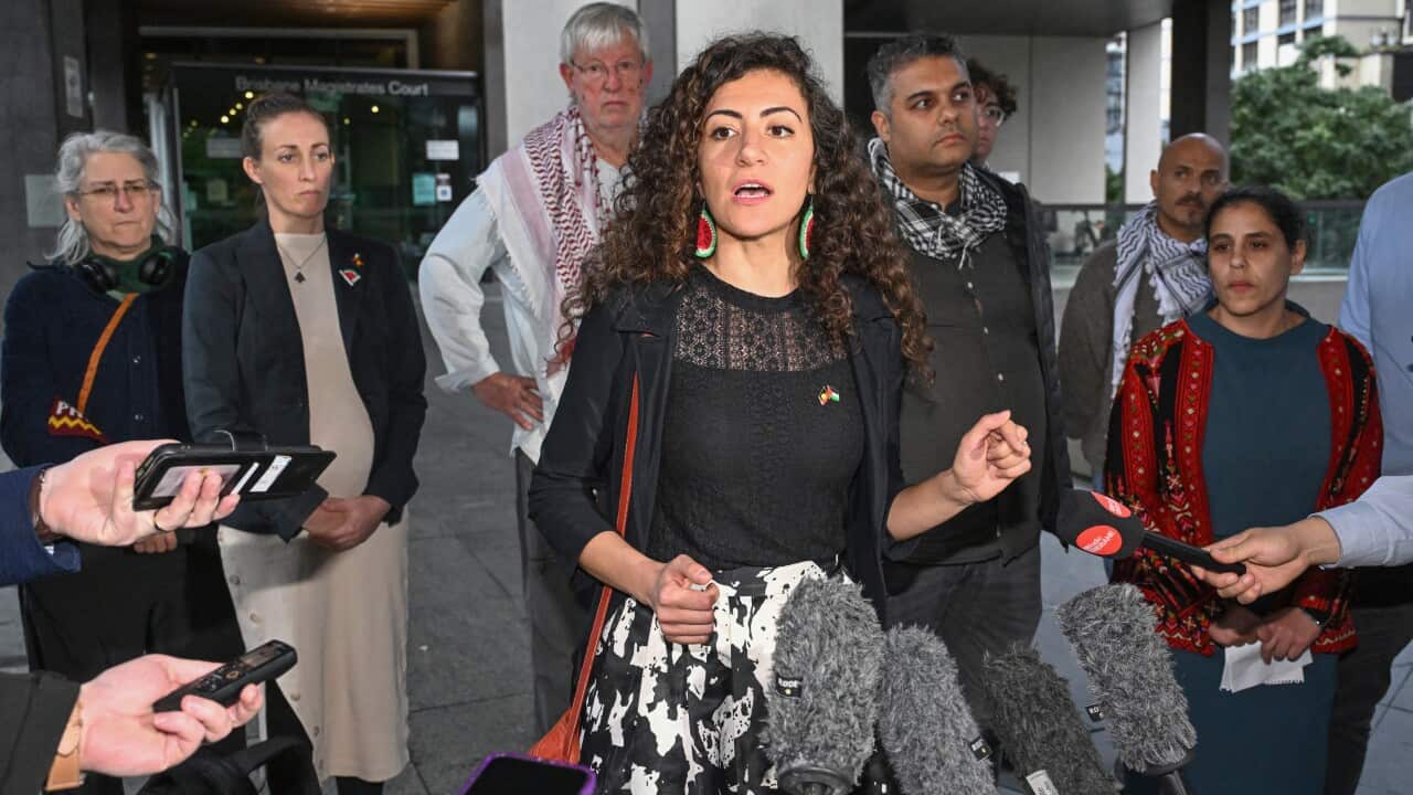 A woman in dark clothing with watermelon earrings speaks in front of a group of people
