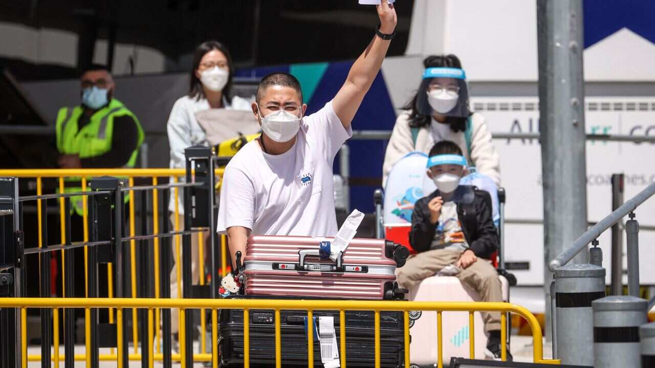Passengers push trolleys carrying their luggage as they prepare to board a bus to take them to mandatory hotel quarantine at the international airport in Sydney