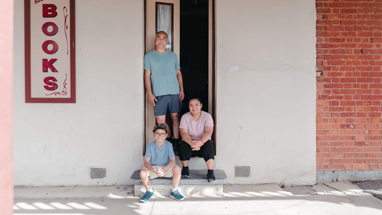 A woman and a boy sit in a doorway in a pale concrete wall. A man standsjust behind them. They all look happy.