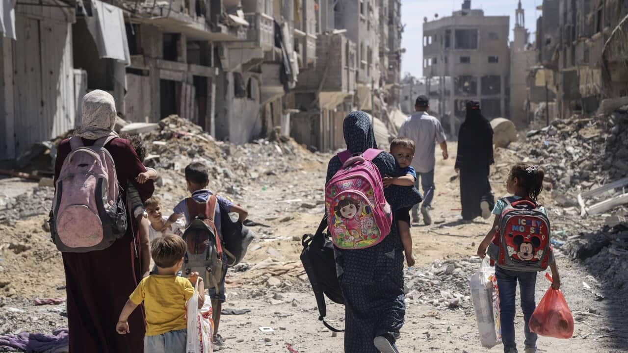 A group of women lead their children down a street with rubble surrounding them.