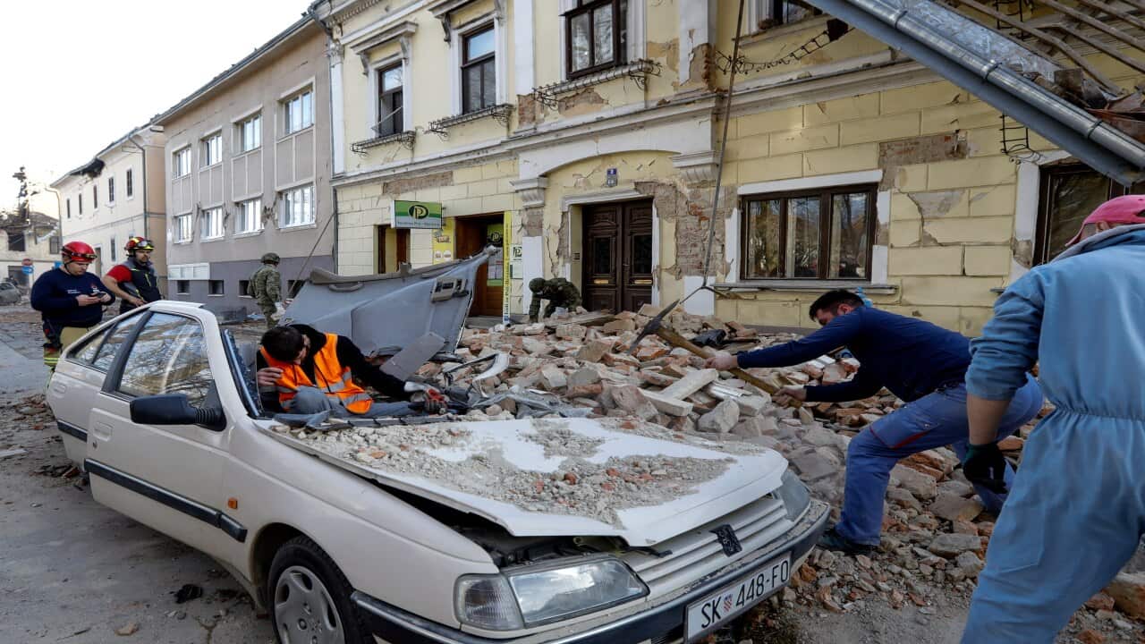 People and soldiers clean the rubble next to car and buildings damaged in an earthquake in Petrinja, Croatia.