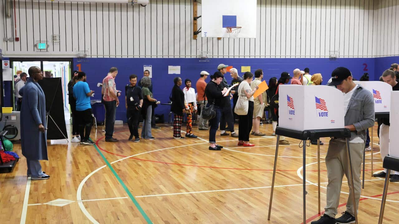 A large group of people standing at a basketball court that's serving as a voting centre.