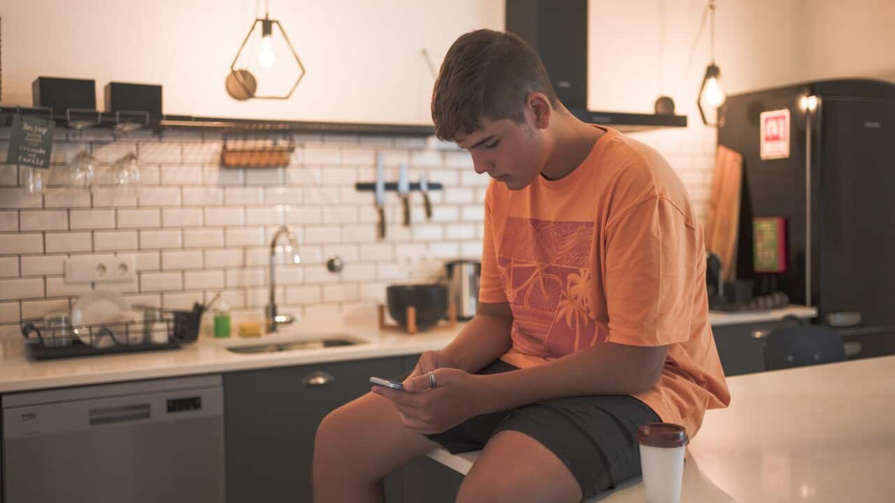Teenage boy sitting at the kitchen table interacting with his smart phone while having a takeaway coffee