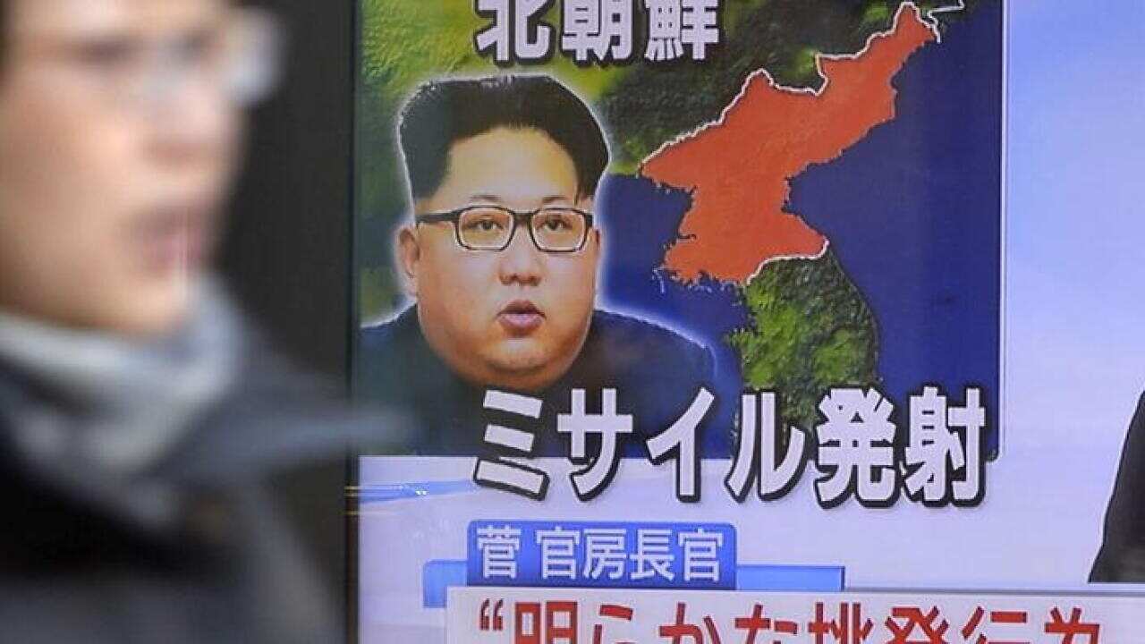 A woman walks past a TV screen showing news on a missile launch by North Korea with a photo of leader Kim Jong Un.