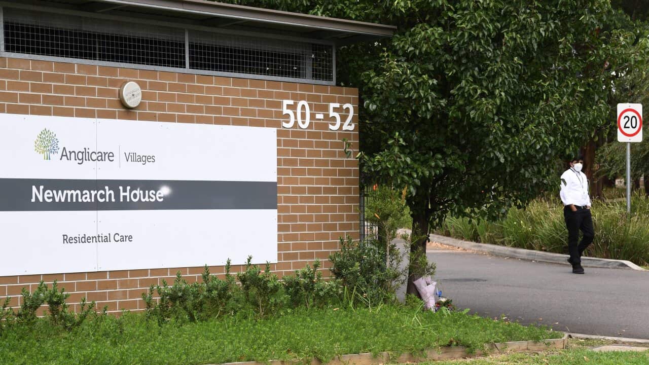 A security guard stands in the driveway as flowers are seen left at the entrance to Anglicare Newmarch House aged care home in Kingswood, Sydney.