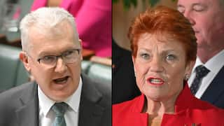 Split image showing two politicians speaking. On the left, a person with short grey hair and glasses wears a dark suit, white shirt and patterned green tie while speaking in parliament. On the right, a person with short red hair wears a red jacket and lipstick while speaking at a media event, with blurred figures in the background. A black vertical line separates the two images.