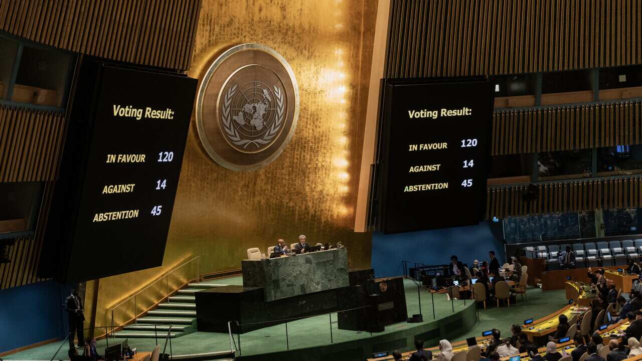 People sitting on podiums in a large room with the United Nations logo on the wall and big screens.