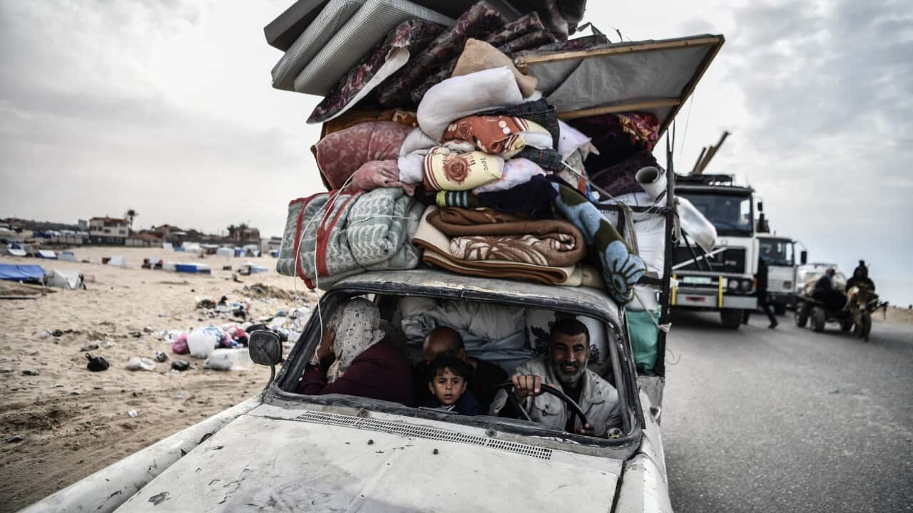 A Palestinian family in the front seats of a car with a roof piled high with mattresses and other household items.