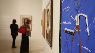 Visitors view artworks inside a gallery exhibition space, including a large blue portrait painting in the foreground.
