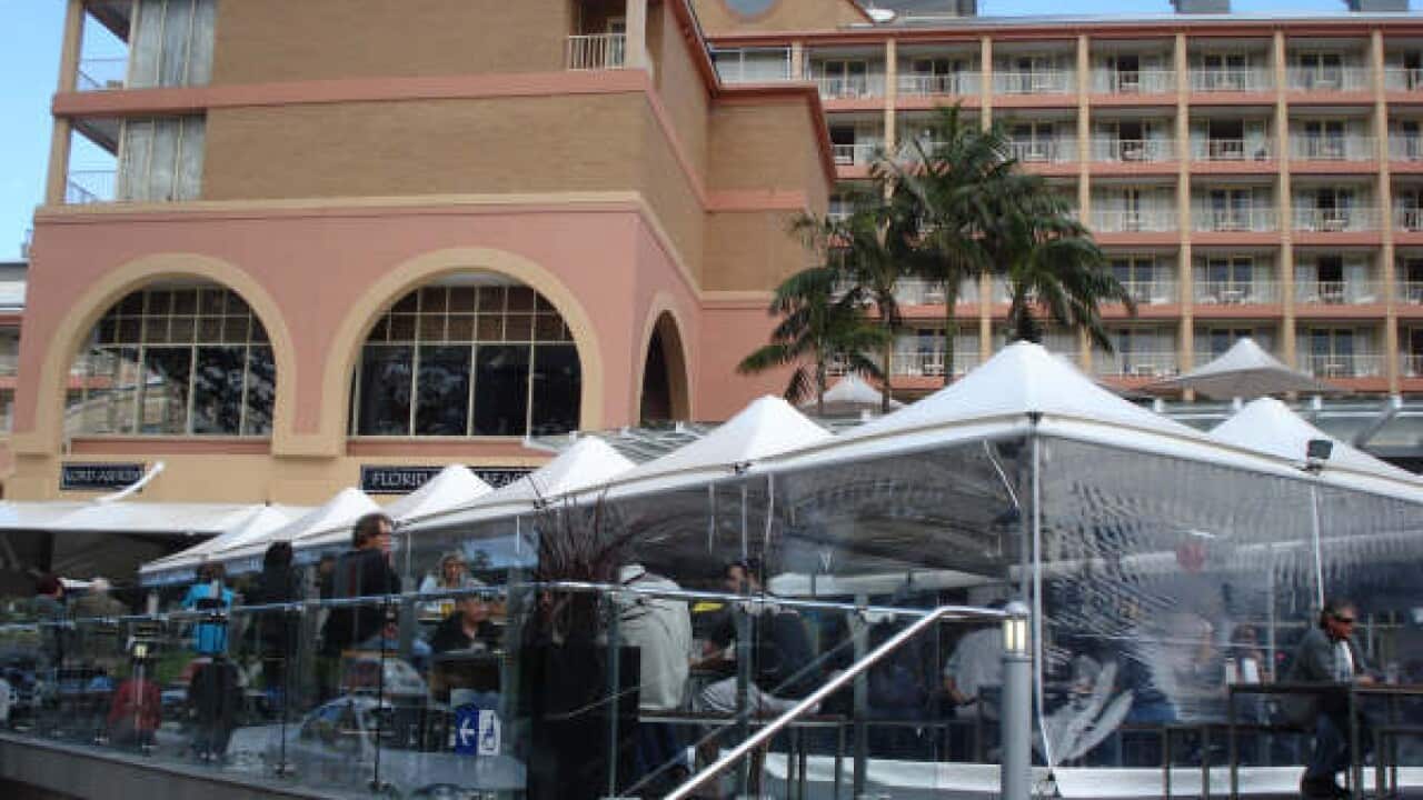 An exterior view of the crowne plaza hotel, with shaded outdoor eating areas in front.