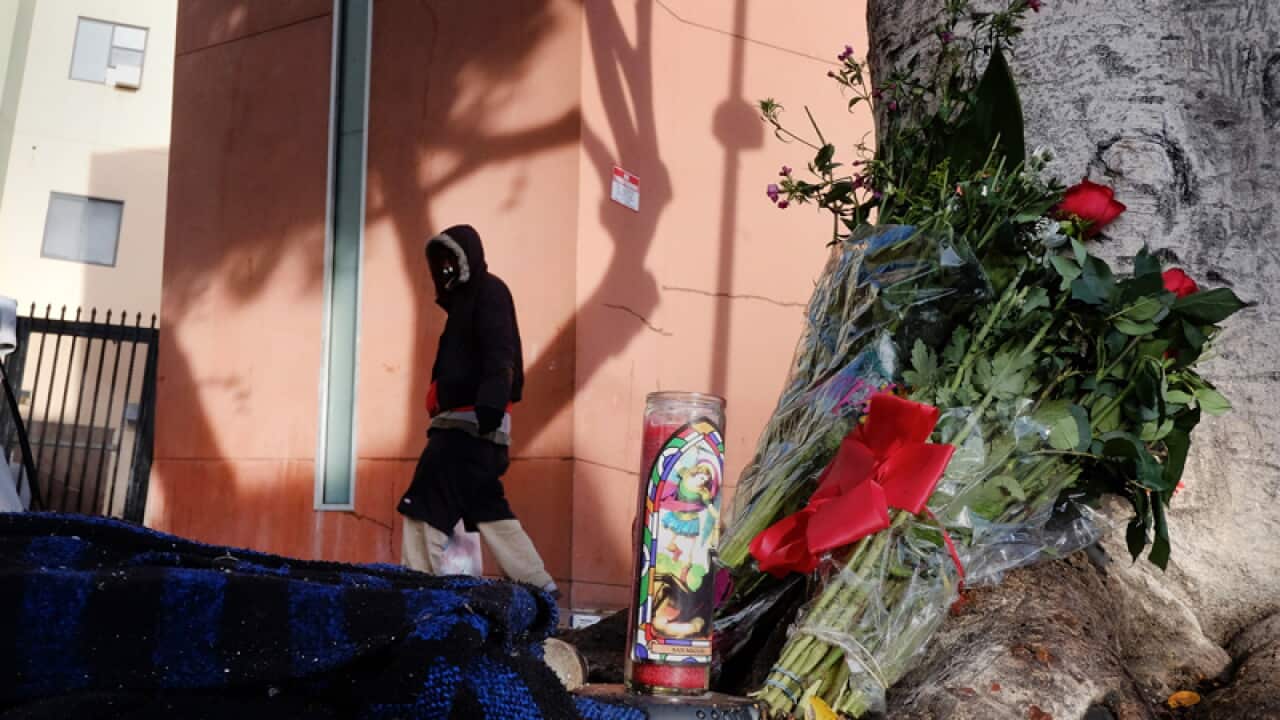 A pedestrian walks past flowers and candles where a man was shot